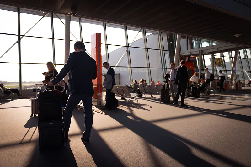 Viajeros con equipaje cruzan la terminal de un aeropuerto a contraluz.